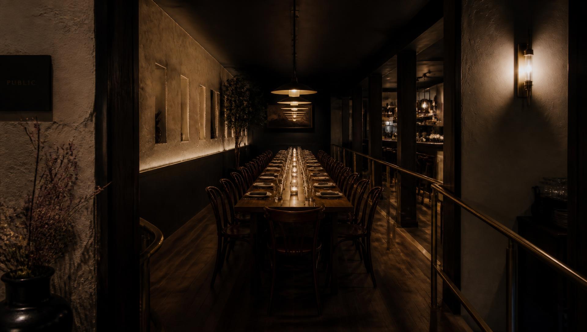 The long communal table set beneath low pendant lights before service